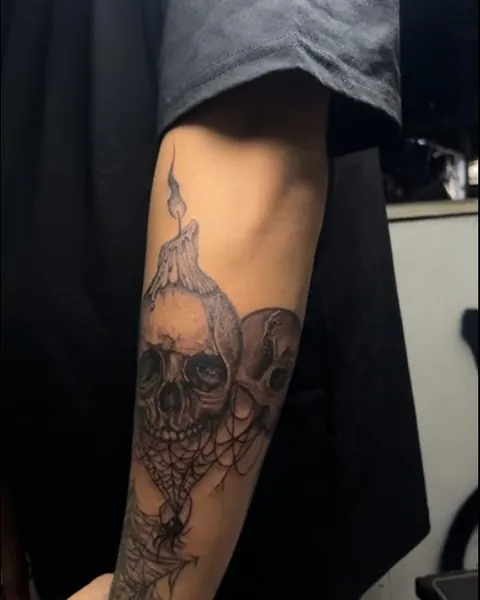 Black and grey forearm tattoo of two skulls under a melting candle with a spiderweb