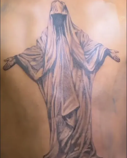 Large black and grey tattoo of a robed figure with open arms across the upper back